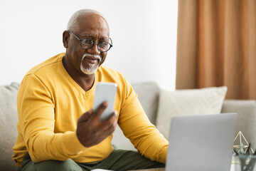 Wall Mural - Mature African American Businessman Using Cellphone And Laptop Working Indoors