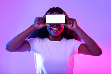 Wall Mural - Smartphone screen mockup. Black woman covering eyes with empty phone, offering space for mobile app in neon light