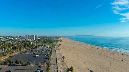 a breathtaking aerial shot of the coastline with vast blue ocean water, silky brown sand and a beachfront cityscape with buildings and palm trees and blue sky at Santa Monica Beach in California USA
