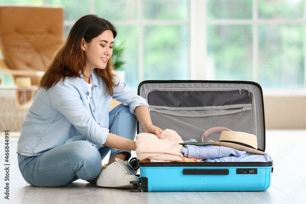 Young woman packing suitcase at home