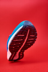 Wall Mural - Blue running sneaker on red background. Sport male shoe steps on red background. Fitness concept