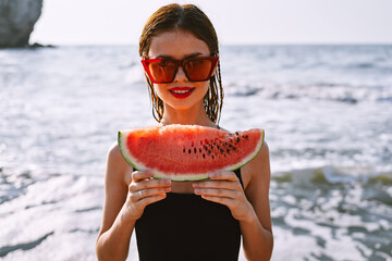 cheerful woman in sunglasses eating watermelon by the ocean