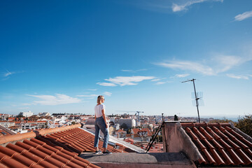 Wall Mural - Traveling by Portugal. Young traveling woman enjoying old town Lisbon view on red tiled roof.