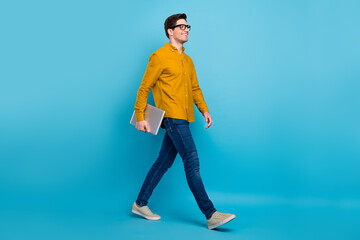 Profile photo of guy walk hold netbook enjoy stroll wear yellow shirt jeans shoes isolated blue color background
