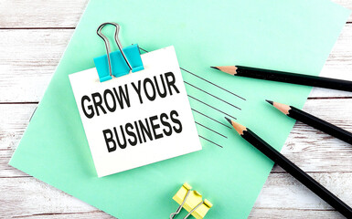 Poster - Text GROW YOUR BUSINESS on the short note with pencils on the wooden background