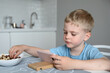 © RinaChu - Cute little boy blonde looks at the smartphone sitting oat the table at home. Concept online education, learning, games.