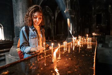 A woman puts a candle and prays in a church or Catholic church. The concept of sorrow and hope in faith
