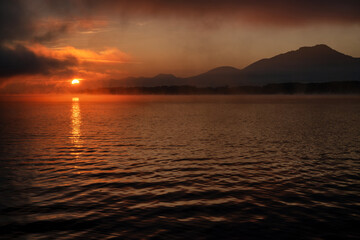 Wall Mural - Colorful sunrise over morning lake. Reflection of orange light from the sun on water level.