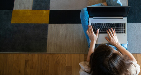Wall Mural - Banner view from above of woman working on a laptop while sitting on the floor.