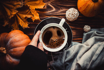 Cup of coffee in hand on wooden brown background with pumkins and leaves