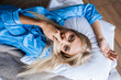 top view of happy blonde woman covering mouth with hair while lying on pillow in bedroom