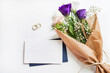 top view of empty card with envelope, flowers and golden wedding rings on white background