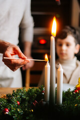 Wall Mural - Vertical blurred close-up shot of young woman lights candles on dinner table served for Christmas family party. Adorable child boy watching preparations for together holidays with parents and friends.