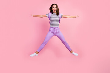 Sticker - Photo of excited funky young lady wear striped outfit backpack smiling jumping high like star isolated pink color background