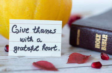 Wall Mural - Give thanks with a grateful heart, a handwritten quote with Holy Bible Book, pumpkin, pomegranate seeds, and red leaves. The biblical concept of thanksgiving to God Jesus Christ. A closeup.