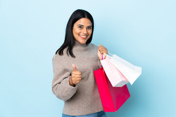 Wall Mural - Young latin woman woman isolated on blue background holding shopping bags and with thumb up