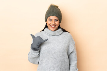 Wall Mural - Young Colombian girl with winter hat isolated on beige background making phone gesture