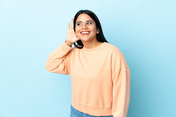 Wall Mural - Young latin woman woman isolated on blue background listening to something by putting hand on the ear