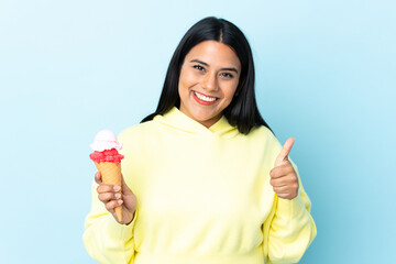 Wall Mural - Young Colombian woman with a cornet ice cream isolated on blue background with thumbs up because something good has happened