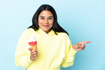 Wall Mural - Young Colombian woman with a cornet ice cream isolated on blue background surprised and pointing finger to the side