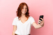 © luismolinero - Teenager reddish woman isolated on pink background making a selfie with mobile phone