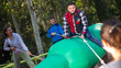Emotional bearded young man sitting astride big inflatable rodeo bottle, having fun with friends in outdoor amusement park
