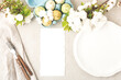 Elegant easter spring table setting design with white blooming flowers, cutlery, empty plate, easter eggs on beige table. Blank card mockup. Restaurant, wedding menu template. Top view, flat lay