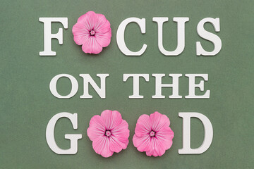 Wall Mural - Focus on the good. Motivational quote from white letters and pink flowers on green background. Creative concept inspirational quote of the day