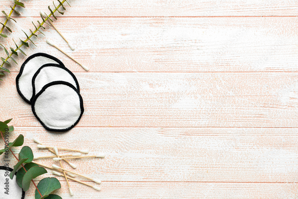 Reusable cotton pads, sticks and eucalyptus leaves on light wooden background