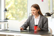 © Pixel-Shot - Young woman working on laptop and drinking coffee in office