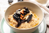 Fototapeta Mapy - Bowl with delicious oatmeal, prunes and almond nuts on table, closeup