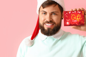 Sticker - Handsome man in Santa hat with gift card on pink background