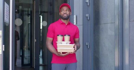 Wall Mural - upset courier man of african appearance leaving house after unsuccessful delivery, holding orders fast food boxes and cups of coffee in hands, wearing red uniform and cap. fast delivery service