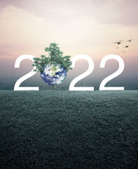 2022 white text with planet and tree on green grass field over aerial view of cityscape at sunset, vintage style, Happy new year 2022 ecological cover, Save the earth concept, Elements of this image f