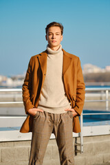 Wall Mural - Young man with hands in the pockets in checkered trousers, sweater and wool coat outdoor