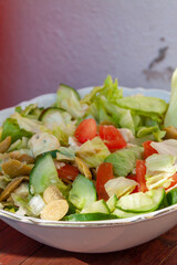 Wall Mural - Vertical shot of a salad with sliced cucumbers, tomatoes, lettuce and mushroom in a white bowl