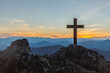 Silhouettes of crucifix symbol on top rock mountain with bright sunbeam on the sunset sky background