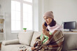 © Studio Romantic - Unhappy woman who has flu or bad cold calling doctor. Sick young lady wearing warm hat, scarf and plaid sitting on sofa at home, looking at thermometer and making phone call to physician. Copy space