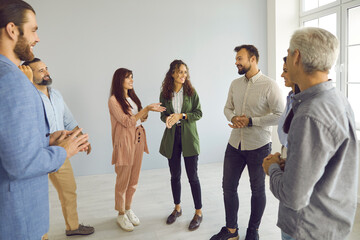 Wall Mural - Happy young and mature people having friendly conversation at business event. Group of men and women meeting with business coach. Team of employees standing in office and having interesting discussion