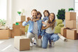 Happy family showing keys to new home on moving day. Portrait of mum, little kids and dad looking at camera and laughing in living room with unpacked cardboard boxes. Buying house or apartment concept