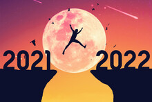 Silhouette Man Jumping And Birds Flying Between Cliff With Number 2021 To 2022 At Top Of Mountain On Sunset Sky Background.