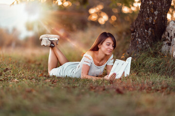 Poster - Shallow focus of a caucasian female with a white dress posing in the park and reading book