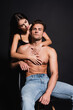© LIGHTFIELD STUDIOS - passionate woman in bra embracing shirtless muscular man sitting isolated on black