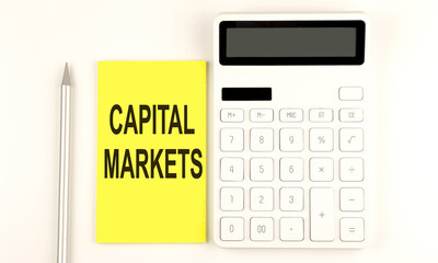 Poster - text CAPITAL MARKETS on yellow sticker, next to pen and calculator