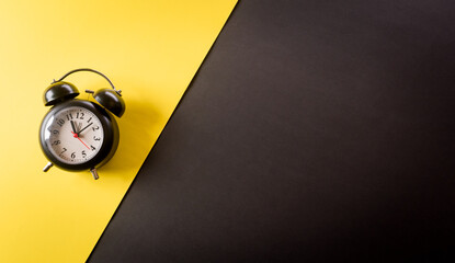 Wall Mural - Top view of black alarm clock on yellow and black background. Shopping concept boxing day and Black Friday composition.
