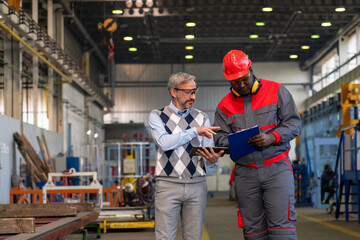 Wall Mural - Caucasian Manager Giving Orders To Black Worker in Protective Workwear With Clipboard - Multiracial Industrial Co-Workers Standing In A Factory And Talking About Production Process