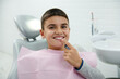© Taras Grebinets - Cheerful boy holds finger near his mouth, looks at camera, smiles with beautiful toothy smile after receiving dental treatment in dentistry clinic. Oral hygiene, early prevention teeth disease concept