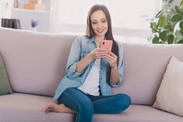 Sticker - Portrait of attractive cheerful long-haired woman sitting on divan using gadget post smm media at light home indoors