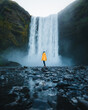 Person in yellow jacket standing near skógafoss waterfall in sk