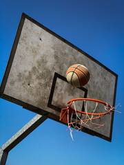 Poster - Vertical shot of a basketball net and ball on a blue sky background